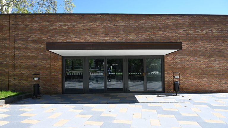A brick facade with large glass doors leading to a building. The ground is paved stylishly, with a clear sky above.