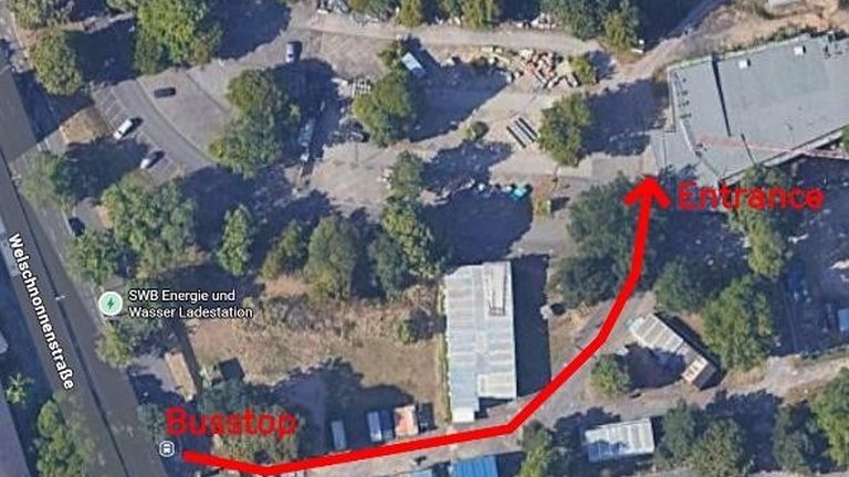 Aerial view of a street with a red line indicating the route from a parking area to a building entrance.
