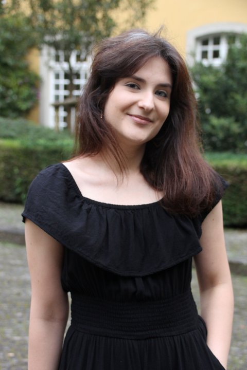 A woman is posing in a dark dress. She is looking into the camera and smiling.