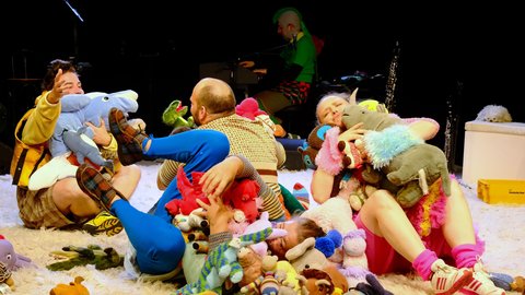 An unconventional stage scene with people and plush toys. The performers appear dressed in colorful, playful costumes. © Claus Overkamp