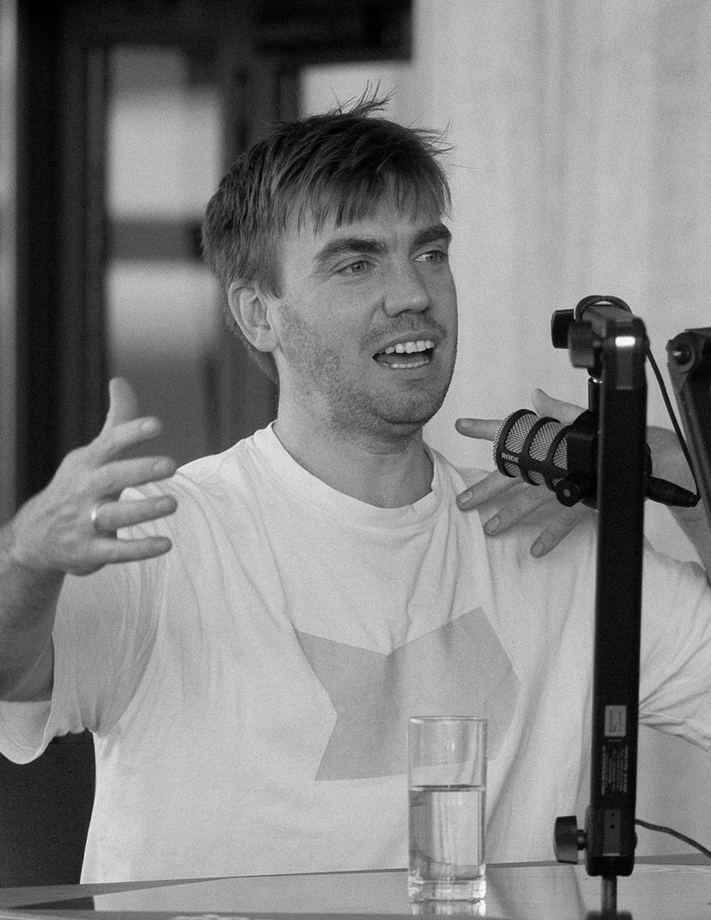Ein Mann ist im angeregten Gespräch und gestikuliert mit beiden Armen. Er trägt ein weißes Shirt.