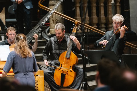 Ein Kammermusikensemble spielt klassische Musik in einem intimen Raum. Die Musiker konzentrieren sich auf ihre Instrumente, darunter eine Geige und Cello.