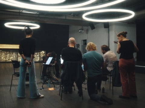 Menschen in einem Raum mit modernen, kreisförmigen Lichtern. Sie konzentrieren sich auf eine Aufführung oder Probe.