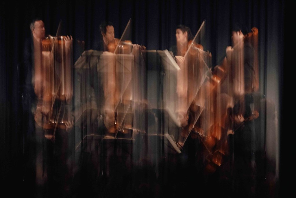 A blurred image of musicians on stage with violins and cello, capturing dynamic movement and energy.