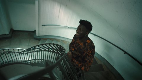 Eine Person in einem gemusterten Hemd steht in einem Treppenhaus. Die Beleuchtung ist gedämpft und erzeugt eine ruhige Atmosphäre.