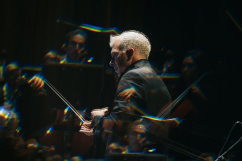 Ein kunstvolles Bild eines Dirigenten im Konzert, überlagert von ein paar Streichern.