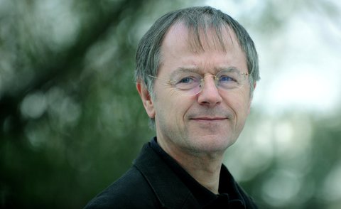 Portrait of a man outdoors in a black suit, with a blurred background of trees or shrubs.  © Wolfgang Schmidt
