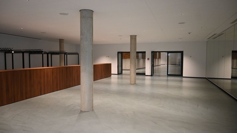 Empty room with gray floor, wooden counter, and pillars. Large window front on the right, modern and minimalist design.