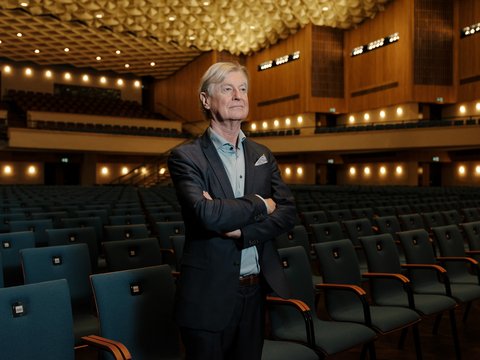 Ein Mann steht mit verschränkten Armen in der leeren, groß beleuchteten Beethovenhalle. Die Sitzreihen sind unbesetzt.