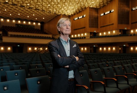 Ein Mann steht mit verschränkten Armen in der leeren, groß beleuchteten Beethovenhalle. Die Sitzreihen sind unbesetzt.