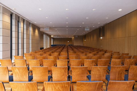 An empty conference room with numerous rows of chairs, well-lit by ceiling lights and large windows on the left side. ©Beethovenhalle Bonn