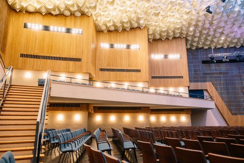 Moderner Konzertsaal mit Holzverkleidung und komfortablen Sitzen. Die Decke hat ein einzigartiges, welliges Design mit vielen Leuchten.