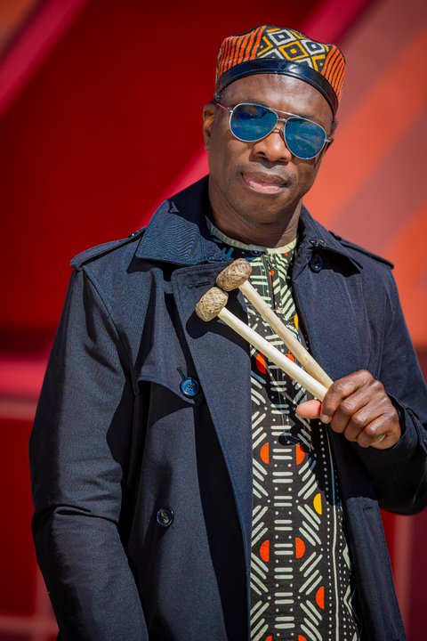 Ein Mann mit Sonnenbrille und traditionellem Hut hält zwei Mallets. Er trägt einen schwarzen Mantel und buntes Hemd.  © Olha Kovalevska (Urban Lys Photos)