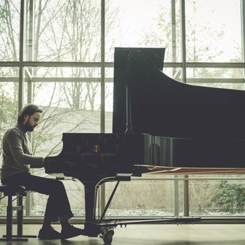 Ein Pianist spielt auf einem Flügel in einem großen, lichtdurchfluteten Raum mit großen Fenstern im Hintergrund.