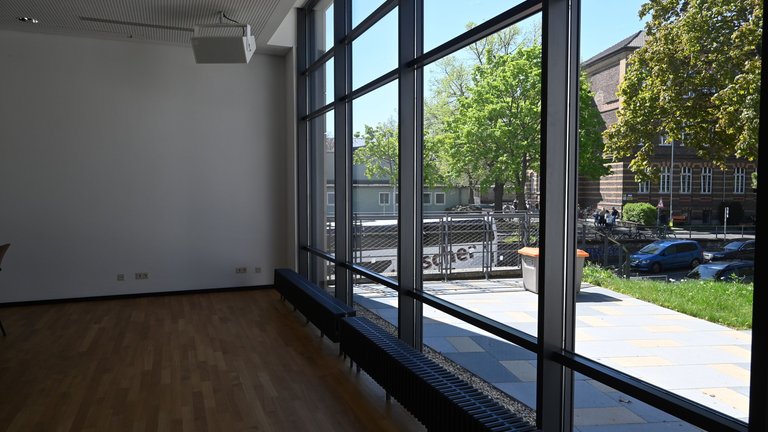 Modern room with large windows offering a view of a sunny street with trees and a building.
