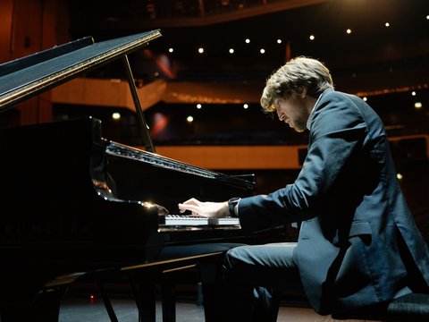 A man is sitting at a grand piano, playing.