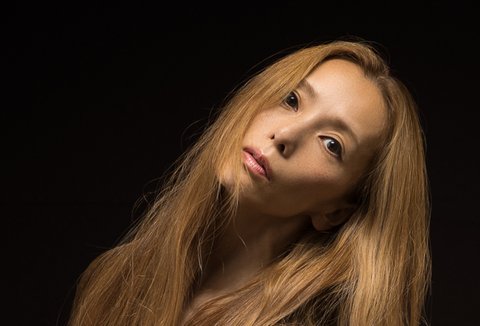 Eine Frau mit langen, fließenden Haaren posiert elegant vor einem dunklen Hintergrund und zeigt anmutige Körperhaltung.