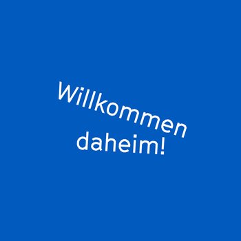 Blauer Hintergrund mit weißem Text in der Mitte: 'Willkommen daheim!' Der Text ist leicht geneigt platziert.