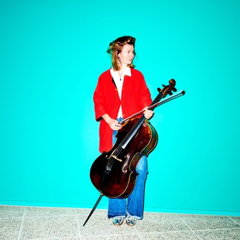 Eine Person in roter Jacke und Jeans hält ein Cello vor einem leuchtend türkisfarbenen Hintergrund. Kühler, minimalistischer Stil.