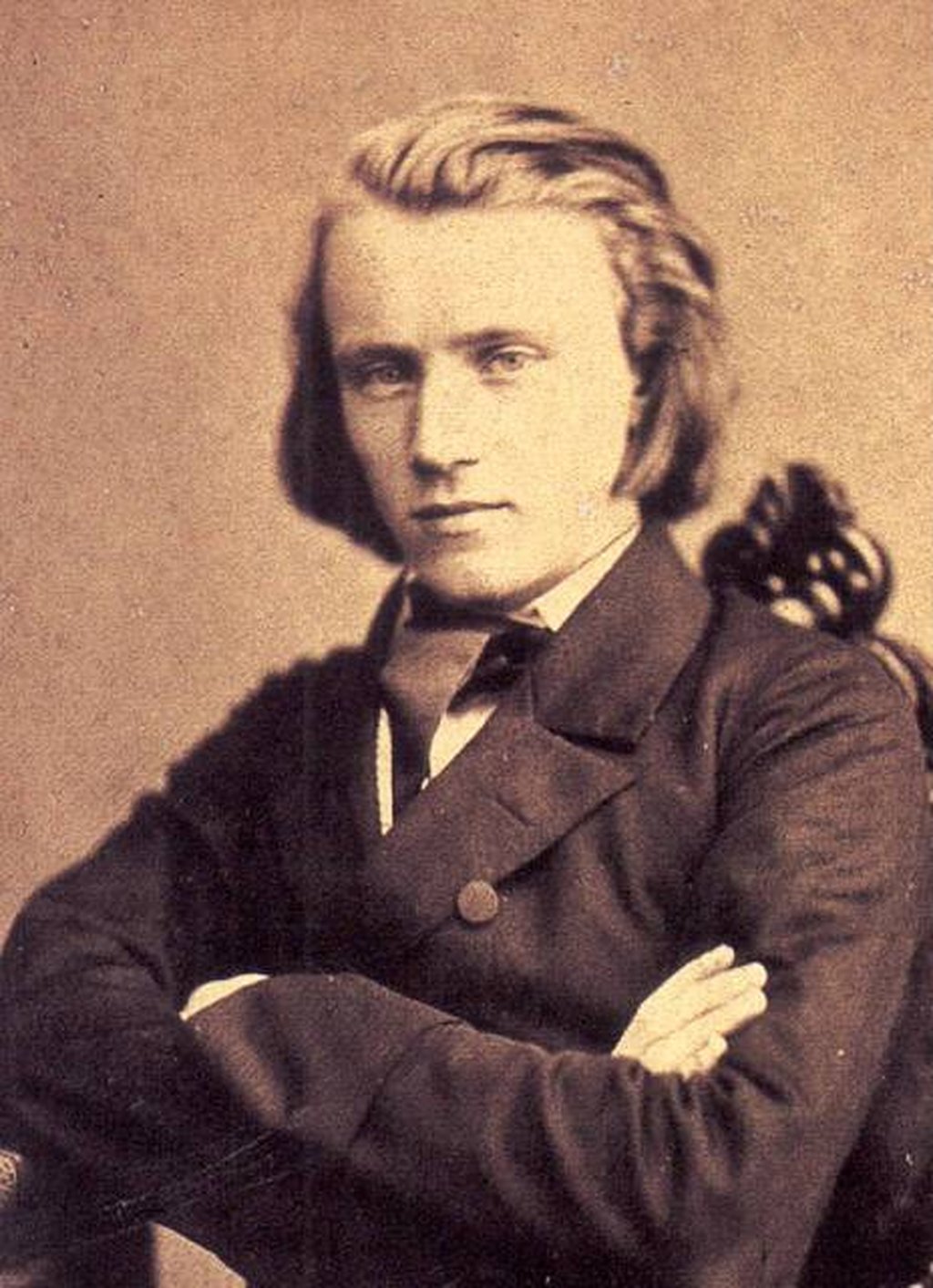 Historische Fotografie eines jungen Mannes mit langen Haaren, der in formeller Kleidung mit verschränkten Armen posiert.