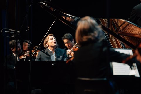 A man is sitting at a grand piano, playing. His head is thrown back, his eyes are closed.