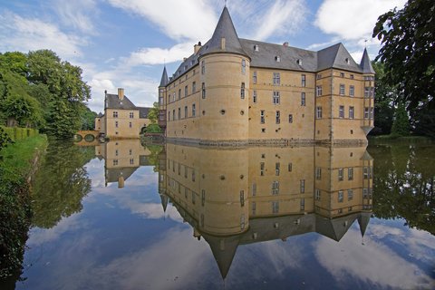 Ein historisches Schloss mit Türmen spiegelt sich in einem ruhigen Wassergraben. Der Himmel ist klar und blau. ©privat