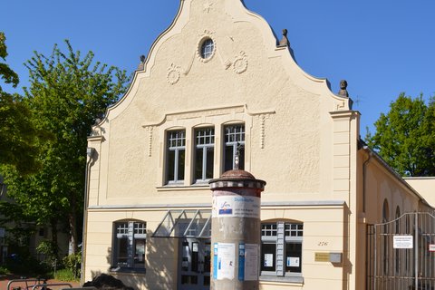 Historisches Gebäude mit einer dekorativen Fassade und einer Werbesäule im Vordergrund. Der Himmel ist klar und blau. ©Enno Schaumburg