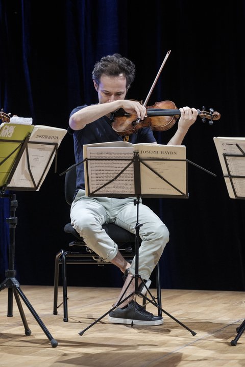 Ein Musiker spielt Geige in einem Ensemble auf einer Bühne. Vor ihm stehen Notenständer mit Notenblättern.