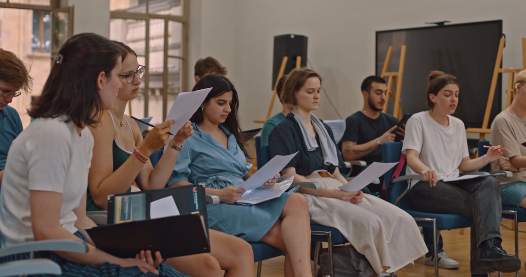 Eine Gruppe von Musiker:innen sitzt in einem Raum mit Noten in der Hand.