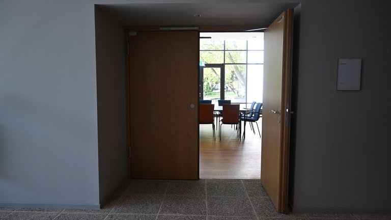 An open door leads into a conference room with chairs and tables. Light streams through the windows in the background.